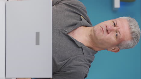 Vertical-video-of-Home-office-worker-man-looks-at-camera-with-happy-and-smiling-face.